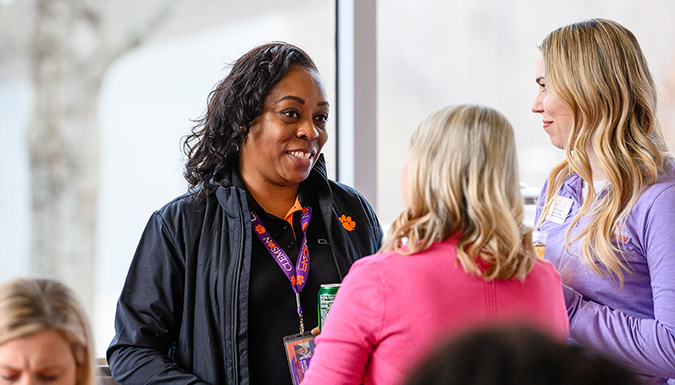 A woman smiles while talking to two other women with their back to the camera.