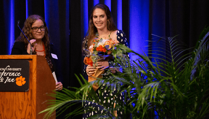 Robyn Curtis presenting flowers to Rhodes Scholar Louise Franke on a stage. 