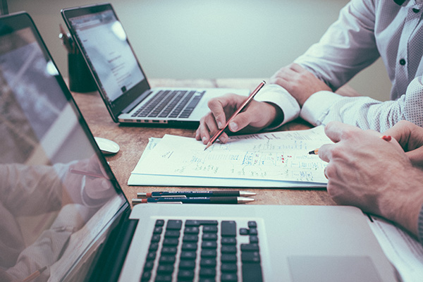 Two people reviewing paperwork placed on a table between two laptops.