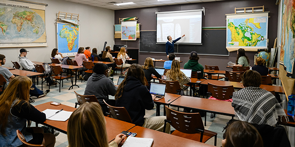 Professor at the front of a full classroom teaching students