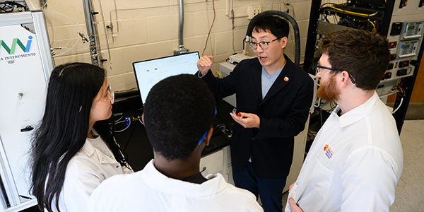 A professor explains a scientific concept to three students in a laboratory setting.