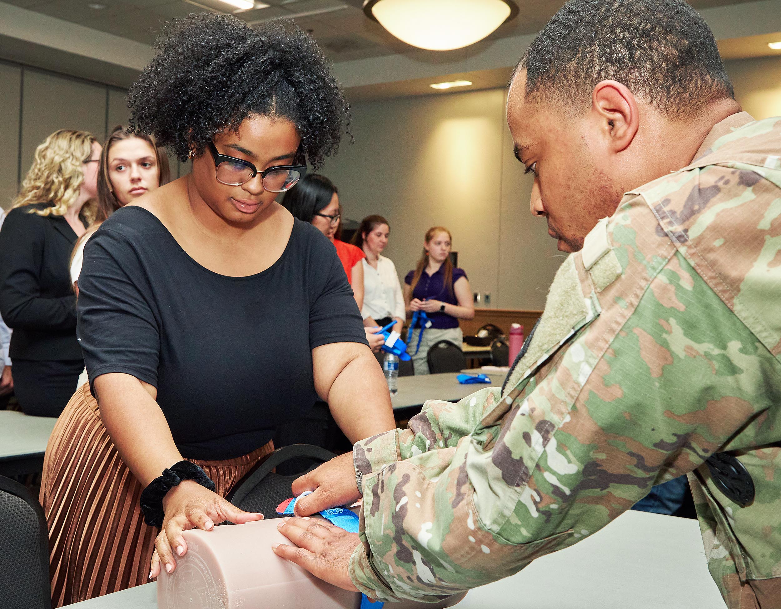 Man in camo outfit assisting woman with a wound-care exercise during a medical training session.