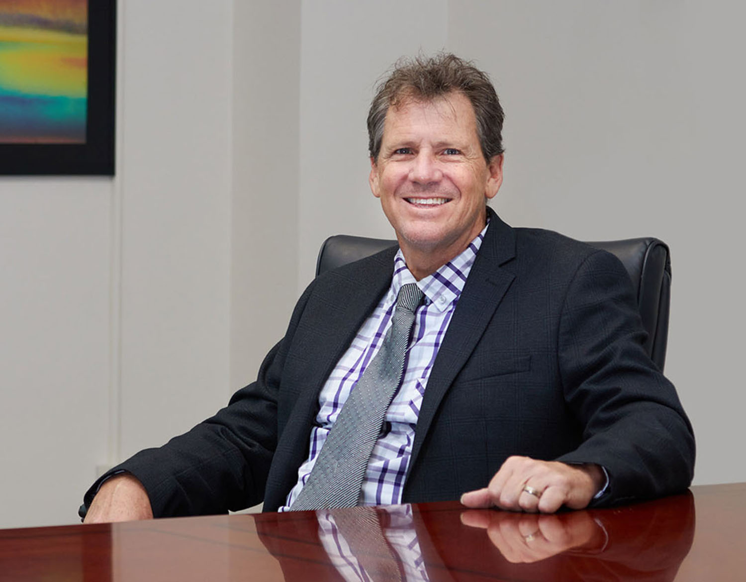 Man, Colin Gallagher, sitting at wood conference table, with one hand on the table.