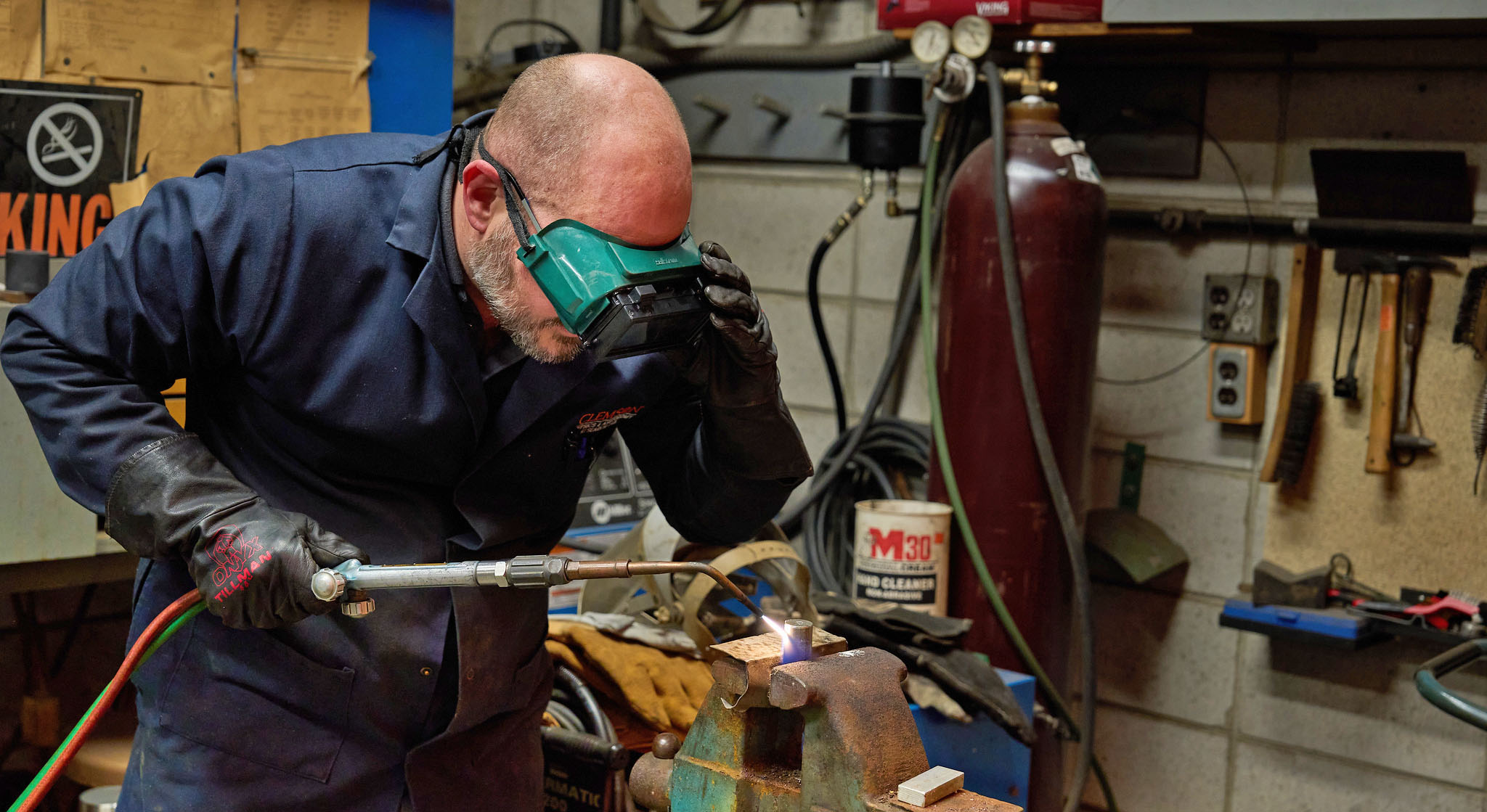 Man wearing goggles using a blowtorch in a machine shop.