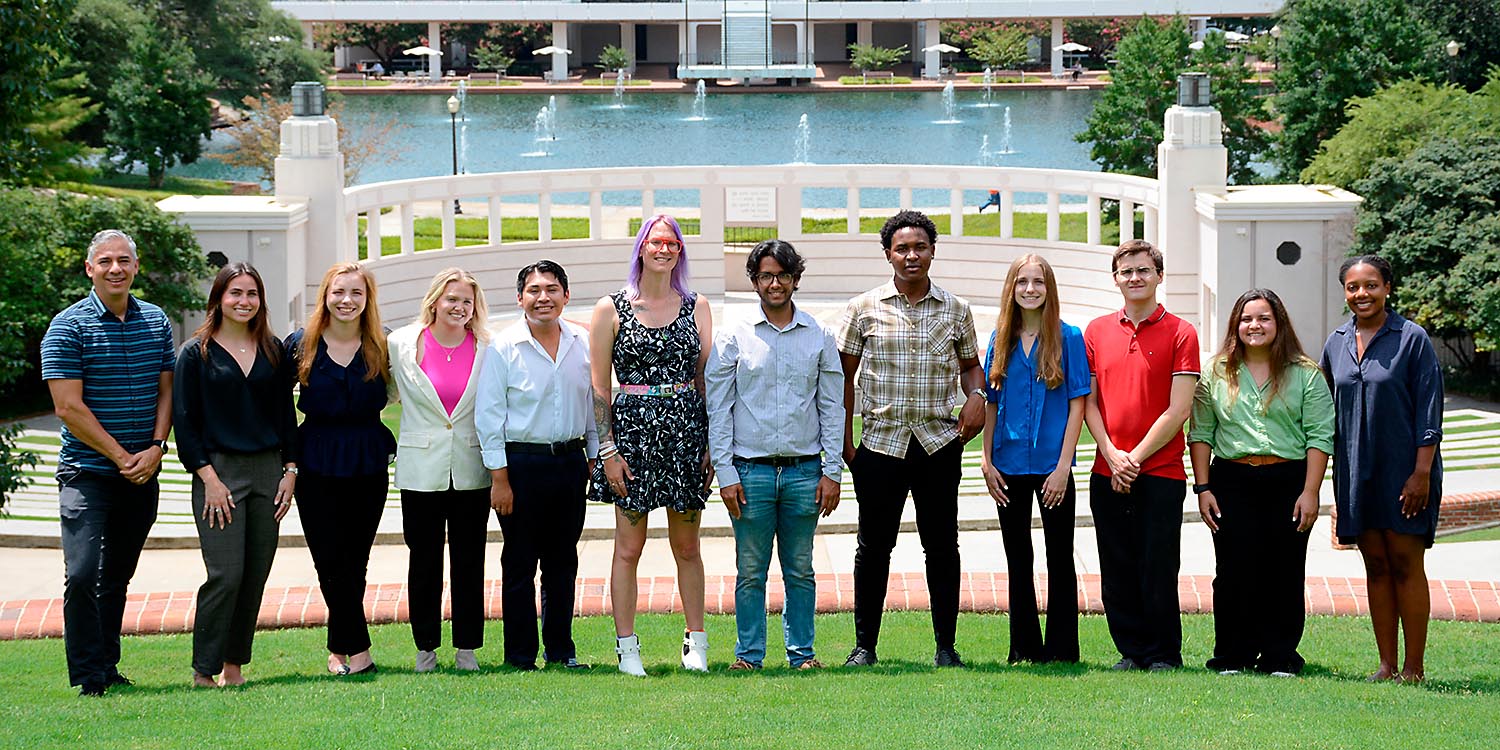 Group of students standing on a lawn with a fountain in the background.