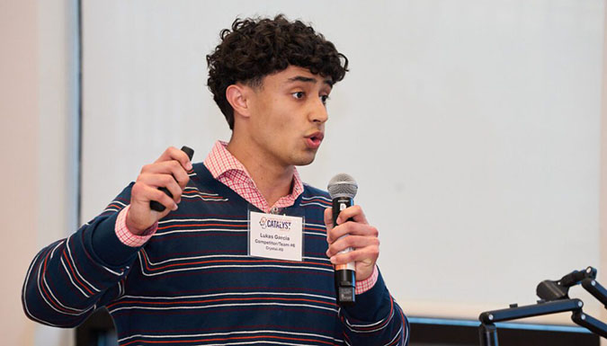 Student, holding a microphone, presenting in front of a video wall.