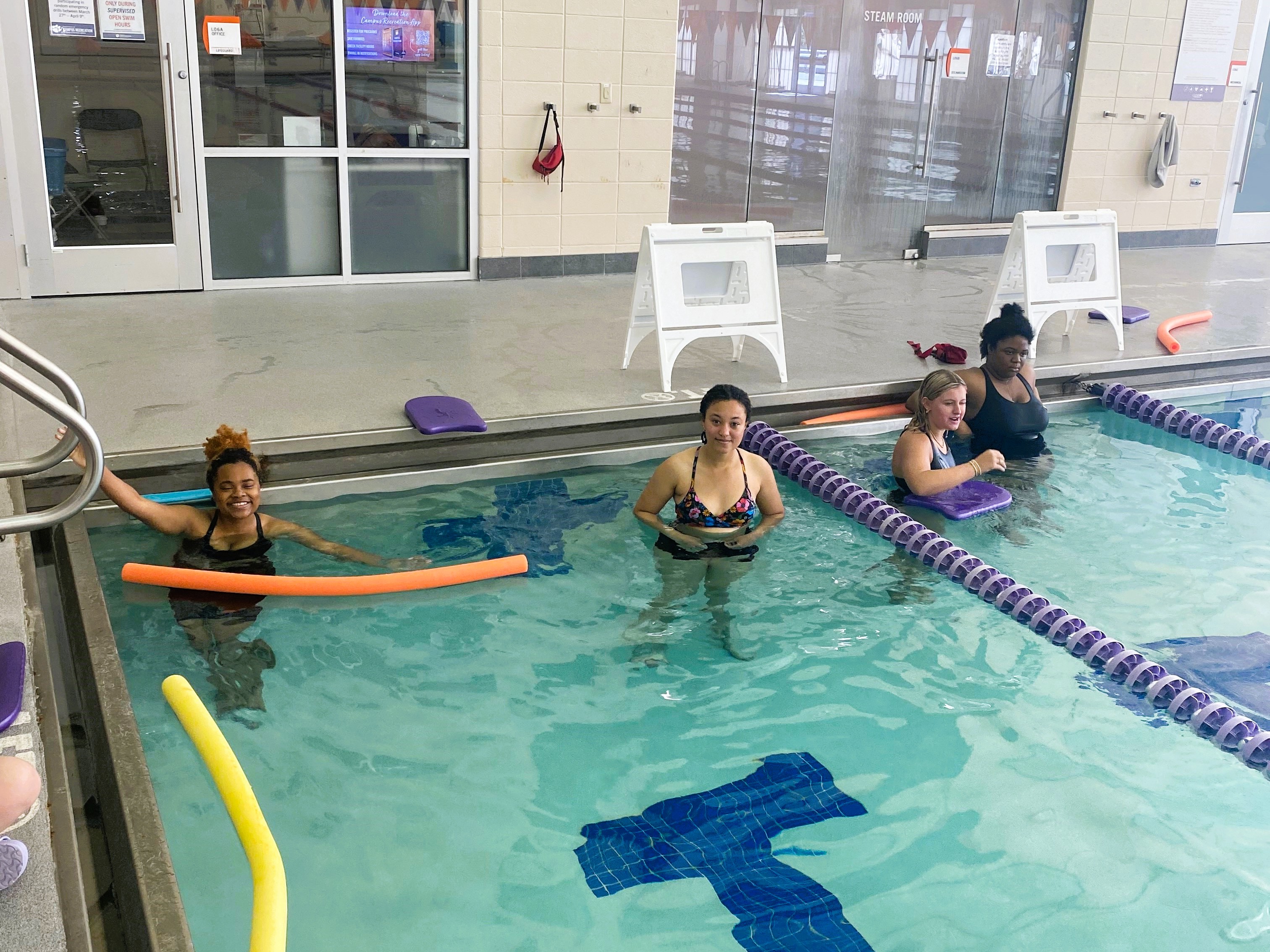 swimmers in a pool with pool noodles floating around them