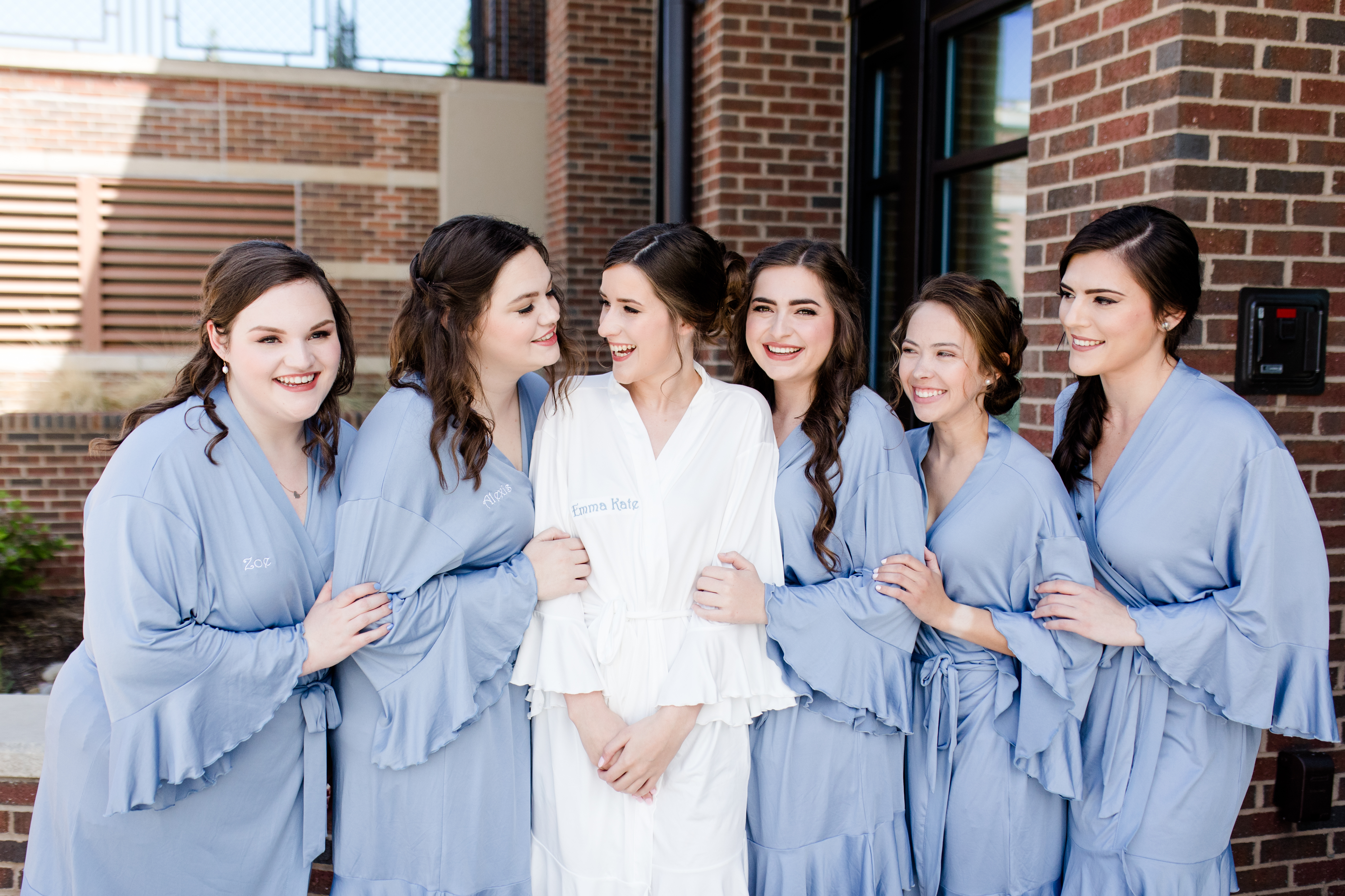 Bride laughing with her bridesmaids in blue and white robes. 