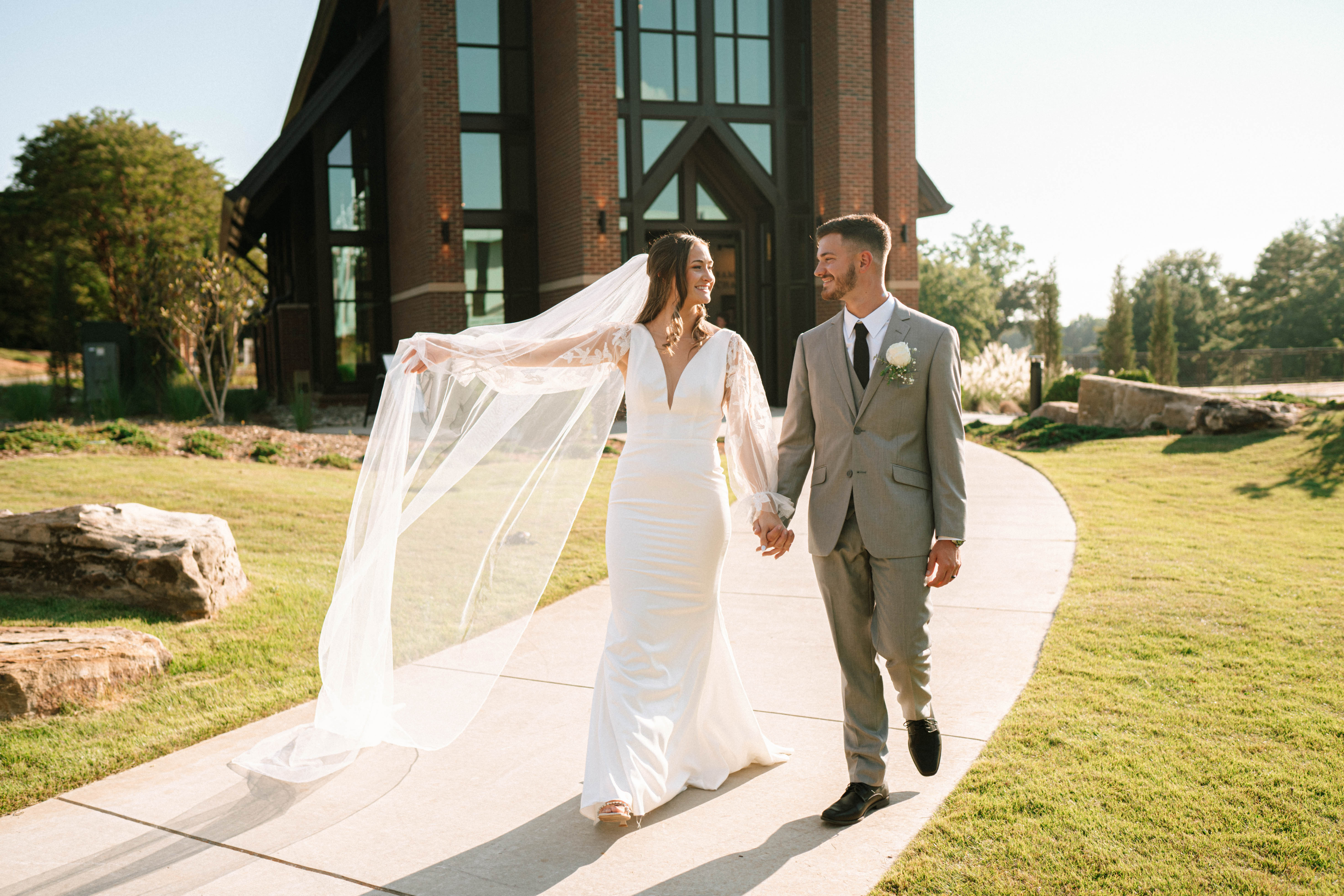 Newly wedded bride and groom walking together after their ceremony outside of the front of the Samuel J. Cadden Chapel.