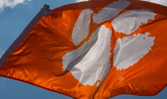 Orange Clemson flag with a white tiger paw flying at the top of a flag pole