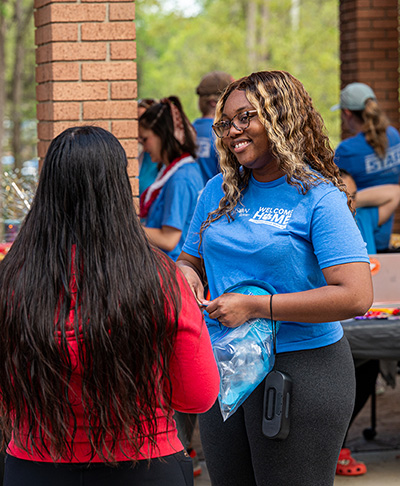 Undergraduate Learning staff member wearing a Welcome Home shirt talks with two students at the Spring Bash.